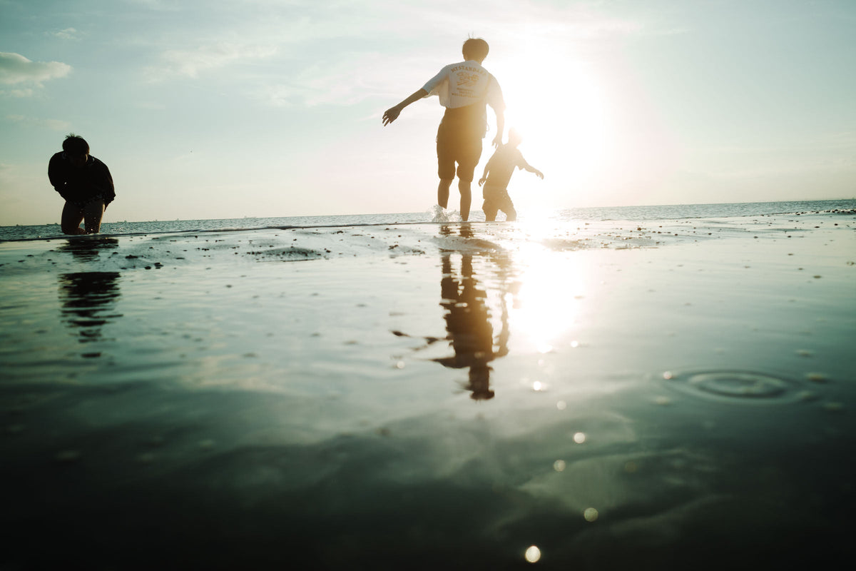 低い太陽に向かって撮った海辺。波打ち際で遊ぶ人たちがシルエットになっている